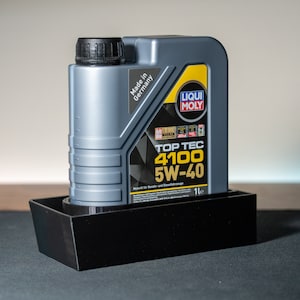 May include: A grey bottle of Liqui Moly Top Tec 4100 5W-40 engine oil with a yellow label. The bottle is sitting on a black plastic tray. The label says "Made in Germany" and "1L".