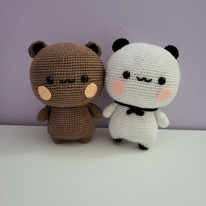 Puede incluir: Dos animales de peluche hechos a mano: un oso marr&oacute;n y un panda blanco. Ambos tienen ojos negros, peque&ntilde;as sonrisas y mejillas sonrosadas. El panda tiene una pajarita negra. El oso tiene mejillas y orejas color canela.