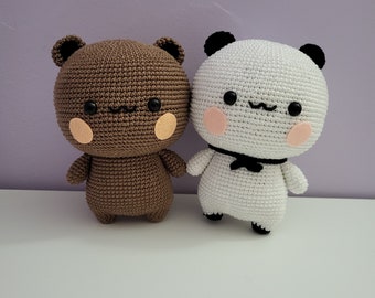 May include: Two handmade crochet stuffed animals: a brown bear and a white panda. Both have black eyes, small smiles, and blush-colored cheeks. The panda has a black bow tie. The bear has tan cheeks and ears.