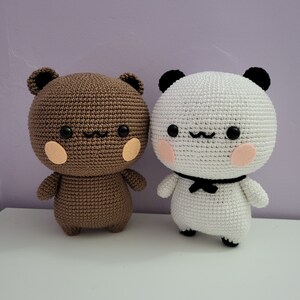 Puede incluir: Dos animales de peluche de ganchillo: un oso marr&oacute;n y un panda. El oso tiene un cuerpo marr&oacute;n, ojos negros y mejillas color melocot&oacute;n. El panda es blanco con detalles negros, ojos negros y una pajarita negra. Ambos tienen brazos y piernas peque&ntilde;os.