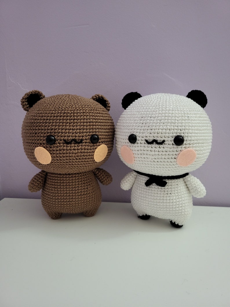 Puede incluir: Dos animales de peluche de ganchillo: un oso marr&oacute;n y un panda. El oso tiene un cuerpo marr&oacute;n, ojos negros y mejillas color melocot&oacute;n. El panda es blanco con detalles negros, ojos negros y una pajarita negra. Ambos tienen brazos y piernas peque&ntilde;os.