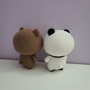 Puede incluir: Dos figuras de ganchillo hechas a mano, un oso y un panda. El oso es marr&oacute;n, y el panda es blanco con detalles negros en las orejas y un collar negro. Ambas figuras tienen orejas peque&ntilde;as y redondeadas y una peque&ntilde;a cola. Est&aacute;n sobre una superficie blanca contra un fondo morado.
