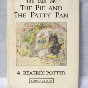 Può includere: La Storia della Torta e della Padella di Beatrix Potter, una copertina di un libro per bambini vintage con un coniglio nero che tiene dei fiori e sta in piedi in una porta.