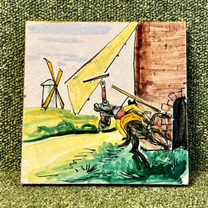 May include: A hand-painted ceramic tile depicting a windmill in a rural landscape. A figure on horseback rides past the windmill, with a yellow sail billowing in the wind. The tile has a rustic, vintage aesthetic.