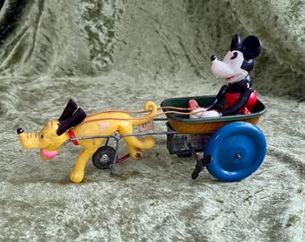 May include: A vintage pull toy featuring a yellow dog with black ears and a red collar, harnessed to a green cart. A black, white, and red Mickey Mouse figure sits inside the cart, which has large blue wheels and a metal frame structure.
