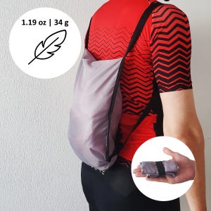 Puede incluir: Una bolsa de compras reutilizable, ligera y de color lila claro, se muestra en la espalda de una persona. La bolsa está hecha de un material fino y duradero y tiene una correa negra. La bolsa se muestra tanto en uso como plegada. La bolsa pesa 34 g.