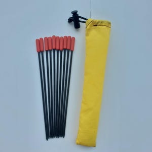 May include: A set of ten thin black metal stakes with bright orange caps arranged in a fan shape, accompanied by a long, rectangular yellow fabric storage pouch featuring a black drawstring closure with a plastic toggle at the top end.