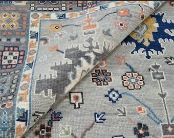 May include: A close-up of a gray rug with a geometric pattern. The rug has a variety of colors, including blue, orange, and yellow. The rug is folded in half, showing the pattern on both sides.