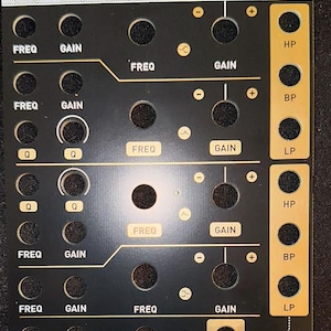 May include: Black modular synthesizer panel with gold lettering and accents. Features knobs, jacks, and labels including "FREQ," "GAIN," "HP," "BP," and "LP." The panel has multiple holes for component mounting and connections.