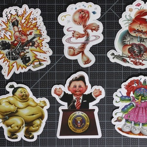 May include: Six colorful stickers featuring cartoon characters with various expressions and poses. The characters are all wearing different outfits and have unique features, such as a large head, multiple eyes, or a missing body part. The stickers are printed on white paper and have a glossy finish.