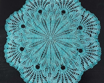 May include: A teal blue crocheted doily with a circular design and a scalloped edge.