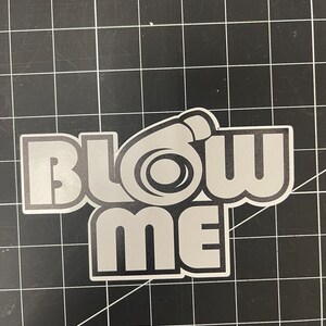 May include: A white vinyl sticker with the text "Blow Me" in black outlined letters. A stylized turbocharger graphic is incorporated into the "O" of the word "Blow".
