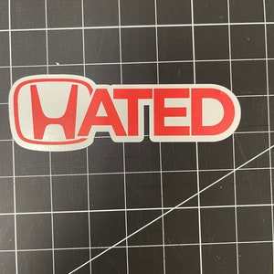 May include: A red and white sticker with the word "HATED" in bold red letters. The "H" is inside a stylised Honda logo.