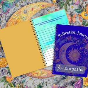 Puede incluir: Una colección de diarios con diseños de mariposas y flores. Un diario es de color amarillo mostaza, otro tiene una cubierta azul con el texto "Reflection journal for Empaths", y el tercero tiene una cubierta turquesa con páginas rayadas.