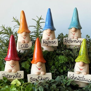 Könnte beinhalten: Sechs Keramik-Gartenzwerge mit spitzen Hüten in Rot, Orange, Blau, Hellblau und Limettengrün. Jeder Zwerg hält ein rechteckiges Schild mit der schwarzen Aufschrift Dill, Majoran, Pfefferminze, Petersilie, Basilikum oder Schnittlauch.