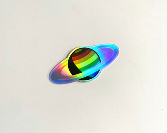 Könnte beinhalten: Ein regenbogenfarbener Planet mit einem Ring darum. Der Planet und der Ring sind schillernd.