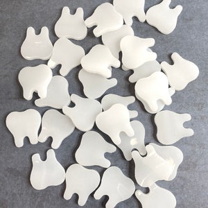 May include: A pile of white tooth-shaped resin charms. The charms are smooth and have a slightly translucent appearance.