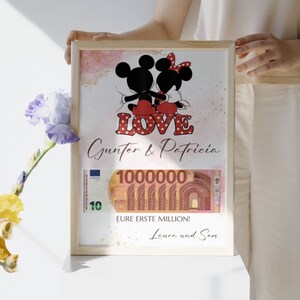May include: A framed print with a pink and gold watercolor background featuring Mickey and Minnie Mouse in red and black outfits. The text "LOVE" is in red with white polka dots. The names "Gunter & Patricia" are written below the image. A 100,000 Euro bill is partially visible at the bottom of the print with the text "EURE ERSTE MILLION! Laura und Sean".