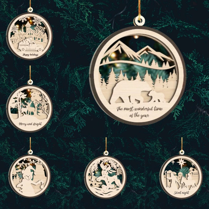 May include: Set of six wooden Christmas ornaments with intricate laser cut designs. Each ornament features a different winter scene, including a snowy village, a forest with deer, a mountain range with bears, a snowman, a reindeer pulling a sleigh, and a nativity scene. The ornaments are decorated with the phrases "Happy Holidays", "Merry and Bright", "The most wonderful time of the year", "Silent Night", and other festive sayings.
