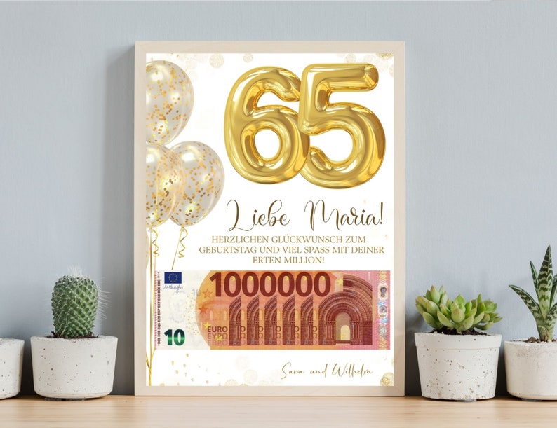 Op de afbeelding: Een ingelijste verjaardagsafdruk met gouden folieballonnen en het getal 65 in goud. De afdruk bevat de tekst "Liebe Maria!" en een afbeelding van eurobankbiljetten ter waarde van 1.000.000. De afdruk is versierd met gouden confetti.