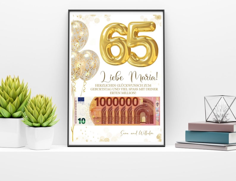 Op de afbeelding: Een ingelijste print met een witte achtergrond toont gouden folieballonnen en het nummer "65" in goud. De tekst "Liebe Maria!" staat boven een afbeelding van eurobiljetten. De print zit in een zwarte lijst.