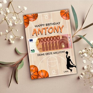 Puede incluir: Una tarjeta de cumplea&ntilde;os con tem&aacute;tica de baloncesto. La tarjeta presenta una cancha de baloncesto con una silueta de jugador de baloncesto, una pelota de baloncesto y un billete falso de 10 euros con el texto "1000000" y "Deine erste Million!" La tarjeta dice "Happy Birthday Antony".