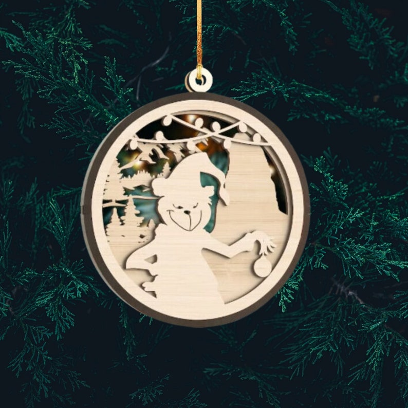 May include: A wooden Christmas ornament featuring a cartoon bear wearing a Santa hat and holding a small ornament. The ornament is decorated with a festive scene of a forest and lights.