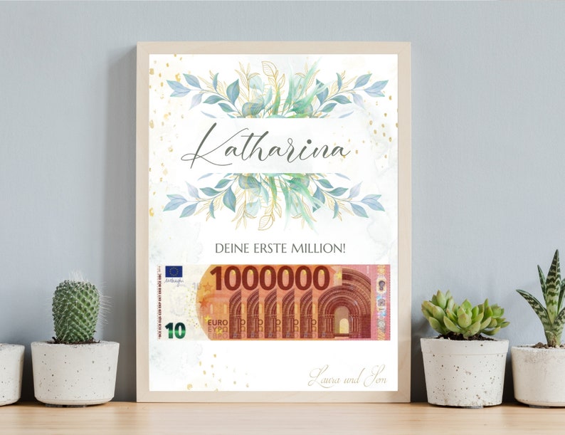 May include: A framed print with a watercolor illustration of green leaves and gold accents. The text "Katharina" is written in a decorative font. The text "Deine erste Million!" is written below the illustration. A mock-up of a 100,000 euro bill is shown below the text. The text "Laura und Tom" is written at the bottom of the print.