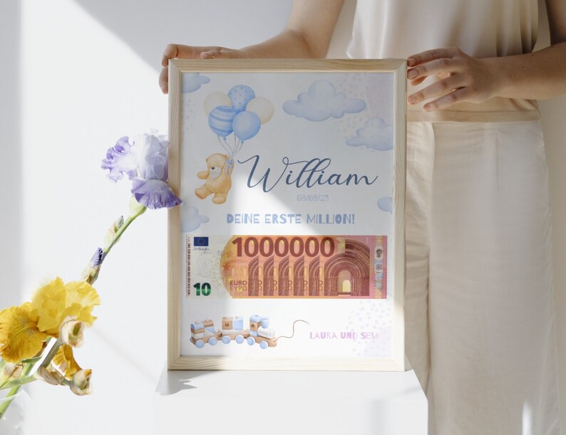 Op de afbeelding: Een ingelijst afdruk met een blauwe en witte aquarel achtergrond. De afdruk toont een teddybeer die ballonnen vasthoudt, een biljet van 10 euro en de tekst "William, Deine Erste Million!" De afdruk is in een houten lijst.
