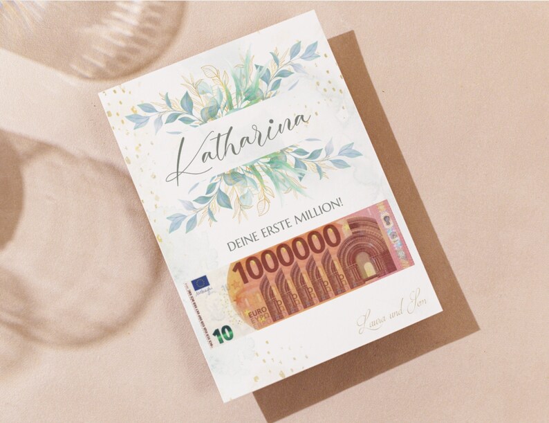 May include: A white card with gold glitter and green watercolor leaves. The card says "Katharina, Deine erste Million!" with a 100,000 euro bill underneath. The card is signed "Laura und Tom."
