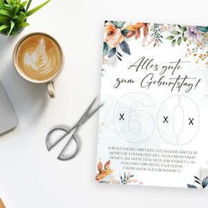 Op de afbeelding: Een witte kaart met een bloemenontwerp en de tekst "Alles gute zum Geburtstag!" met het getal 60 uitgesneden. Het getal 60 heeft lijnen die aangeven waar te knippen.