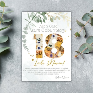May include: A white card with green foliage and gold glitter accents. The number 18 is made of euro bills. The text reads "Alles Gute zum Geburtstag!" and "Liebe Maria!"  "Wir w&uuml;nschen dir viele Momente voller Freude, Gl&uuml;ck und Zufriedenheit. M&ouml;gen alle deine Tr&auml;ume in Erf&uuml;llung gehen und das Leben dir immer wieder sch&ouml;ne &Uuml;berraschungen bereithalten. Bob und Laura"