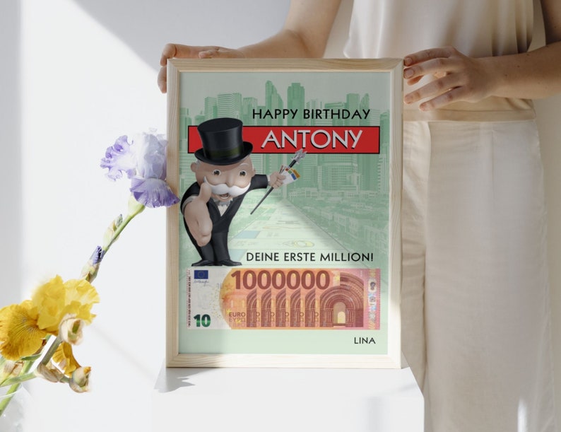 May include: A framed birthday card featuring a cartoon Monopoly Man character with a green background and the text "Happy Birthday Antony. Deine erste Million!" and a 10,000 Euro bill.