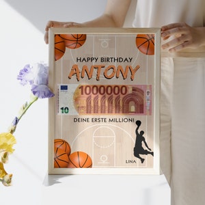 Puede incluir: Una tarjeta de cumplea&ntilde;os enmarcada con tem&aacute;tica de baloncesto. La tarjeta presenta una cancha de baloncesto con un aro de baloncesto, balones de baloncesto y una silueta de un jugador de baloncesto. La tarjeta tambi&eacute;n incluye un billete de dinero falso con el texto "100000" y las palabras "Happy Birthday Antony, Deine erste Million!" y "Lina".