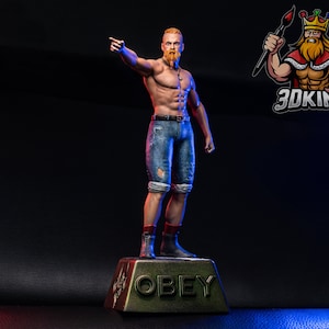 May include: A statue of a muscular man with red hair and a beard, wearing denim shorts and boots, pointing. The base reads "OBEY" in gold lettering. A logo of a king with a crown and paintbrush is in the upper right corner.