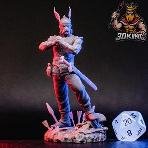 Op de afbeelding: Een grijs plastic miniatuurfiguur van een krijger met hoorns, die een zwaard vasthoudt en op een basis met pijlen staat. Een witte 20-zijdige dobbelsteen met zwarte cijfers bevindt zich op de voorgrond.