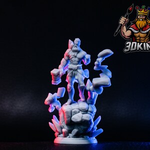 May include: A white 3D printed miniature of a warrior figure standing on a rocky base with crystal-like formations. The figure is holding a hammer in one hand and has a muscular build.