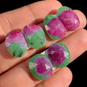 May include: Six oval-shaped gemstones with a vibrant color combination of pink and green. The gemstones are faceted, displaying multiple reflective surfaces. The pink color is concentrated in the center, surrounded by a green border.