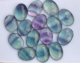May include: A collection of oval gemstones in shades of blue, purple, and clear. The gemstones have a faceted cut, creating multiple reflective surfaces. The arrangement of the stones is scattered, showcasing their varying colours and patterns.