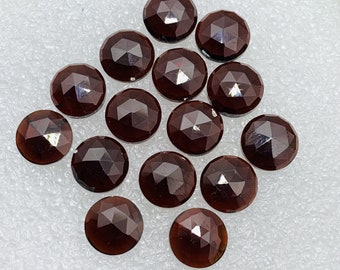 Pode incluir: Uma coleção de 15 gemas facetadas de cor vermelho escuro. As gemas são redondas e têm um acabamento liso e polido.