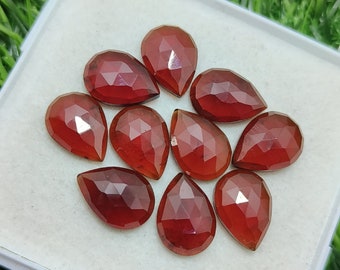 Pode incluir: Dez pedras preciosas facetadas em forma de lágrima em vários tons de vermelho, dispostas em semicírculo sobre uma superfície branca.