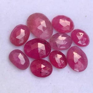 May include: A collection of ten faceted ruby gemstones in various sizes and shapes. The rubies are a deep pink colour and have a smooth, polished finish.
