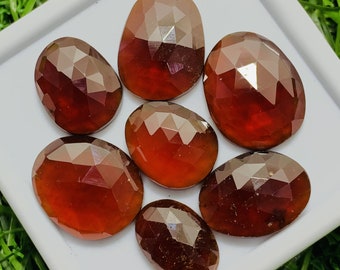 Pode incluir: Sete pedras preciosas facetadas, de forma oval, de cor marrom-avermelhada. As pedras preciosas estão dispostas em um grupo sobre uma superfície branca.