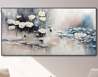 Könnte beinhalten: Ein großer gerahmter Gemälde zeigt weiße und gelbe Lotusblumen auf einem Teich. Das Kunstwerk hat einen strukturierten, dreidimensionalen Effekt mit sanften Pastellfarben. Das Gemälde wird über zwei weißen Sesseln ausgestellt.