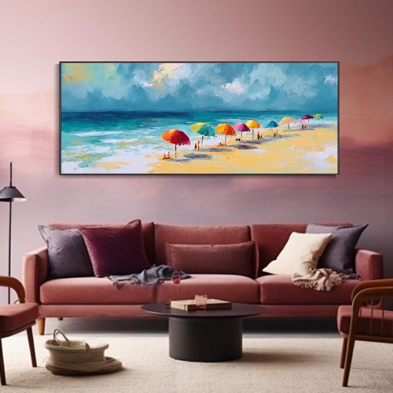 May include: A framed painting of a beach scene. The artwork shows a sunny beach with colourful umbrellas, people, and a vibrant ocean under a cloudy sky. The painting is displayed above a red sofa with cushions.