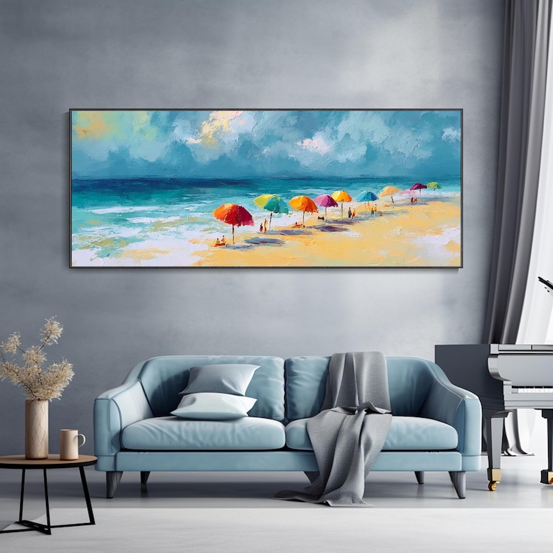 May include: A framed painting of a beach scene. The artwork shows a sandy beach with colourful umbrellas, people, and the ocean under a cloudy sky. The painting is displayed above a blue sofa.