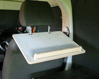 May include: A white wooden desk mounted to the headrest of a car seat. The desk has a small ledge on the front edge. The desk is in a car interior.