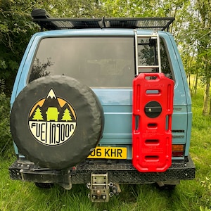 May include: A blue van with a spare tyre on the back. The spare tyre has a black cover with a mountain and trees design and the words "Fuel Injooo". The van has a red fuel container attached to the back.