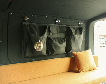 May include: Black canvas storage organizer with multiple pockets, mounted on a dark wall. The organizer has a logo that says "Fuel Road". A tan cushion sits on a matching bench below.