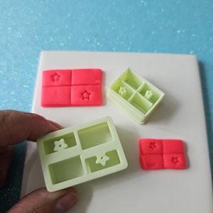 May include: Four-part molds and a star-shaped design. The molds are in shades of pink and green. The molds are on a white surface with a blue glitter background. The molds are for crafting or baking.